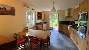 A modern kitchen with wooden cabinets, a dining table with chairs, and a large window providing natural light. - Villa with pool and garden - 30' from Lyon (Saint-Just-Chaleyssin)