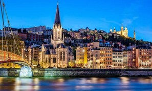 Une vue urbaine avec une église imposante, un pont et des bâtiments le long d’une rivière.