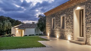 A stone building with a tiled roof, a well-maintained lawn, and a pathway leading to the entrance. - Uddastri Retreat (Arzachena)