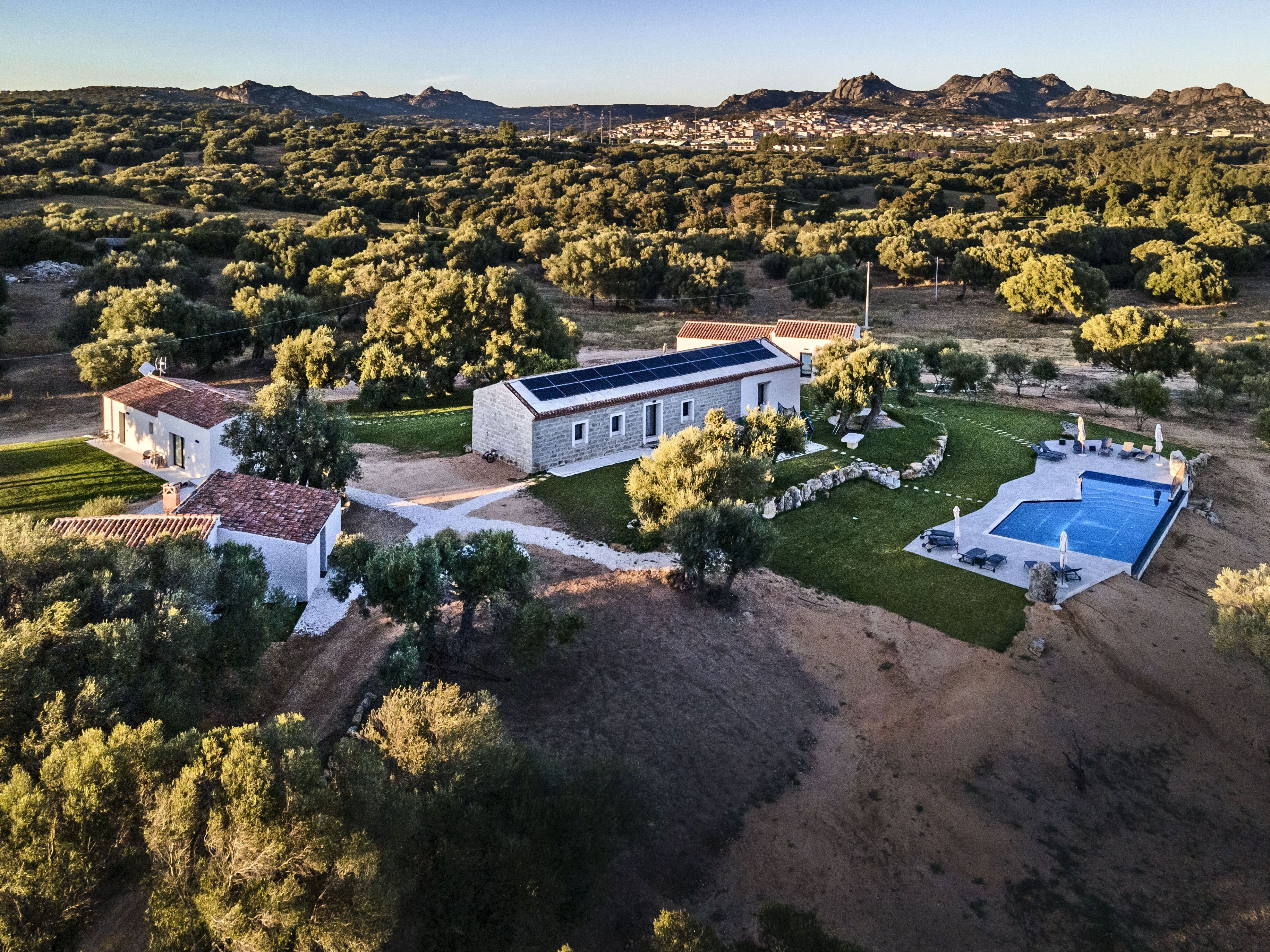 A large house with a swimming pool, surrounded by trees and a hilly landscape.