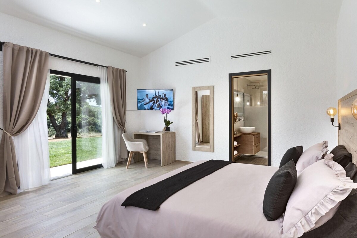 A modern bedroom with a large bed, a desk, and a bathroom visible through an open door.