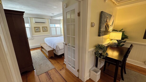 Une chambre à coucher avec un lit, un banc, un bureau avec une lampe et une petite poubelle.