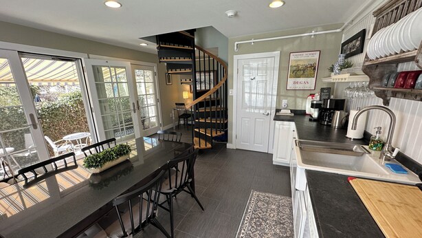 A modern kitchen with a central island, a dining area with chairs, a staircase, and a view through large windows. - Dive into downtown Newport RI in this private, large, unique townhouse-style 2BR apartment at 205 Spring St! King and Full beds + pull-out sofa full kitchen, 2 baths, outdoor patio, AC, TVs, Wifi. Just steps to Thames Street, shops and wharfs (Newport)