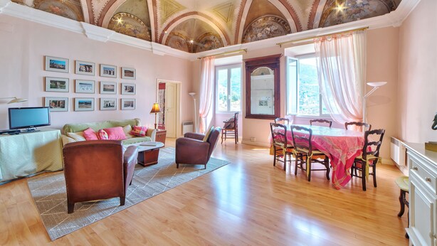 Uma sala de estar ampla com piso de madeira, um sofá, uma mesa de centro e um espaço de jantar com mesa e cadeiras.