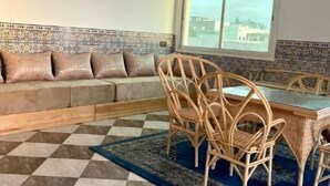 A room with a checkered floor, a sofa with patterned cushions, a dining table with chairs, and a hanging light fixture.
