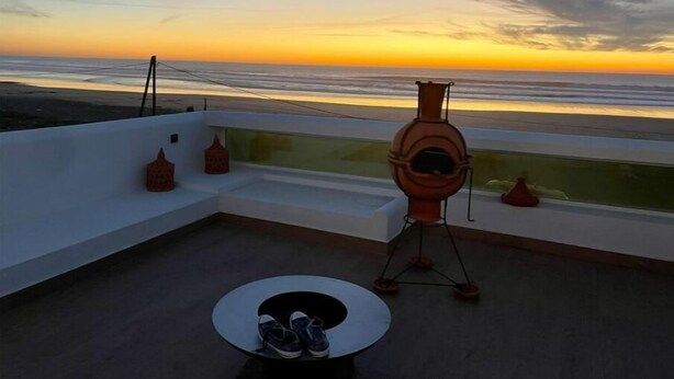 A rooftop terrace with a view of the sunset over the ocean, a telescope, and a small table with shoes.