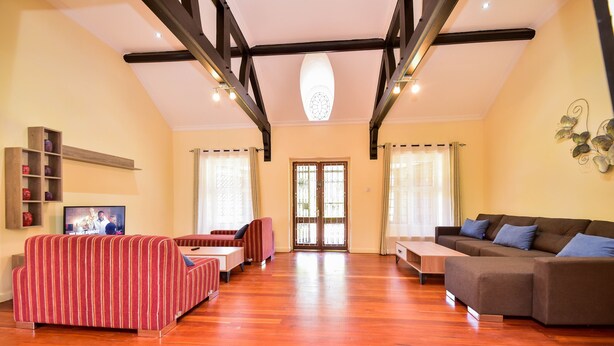 Un salon spacieux doté d’un parquet en bois, d’un grand canapé, d’un canapé plus petit à rayures et d’un téléviseur fixé au mur.