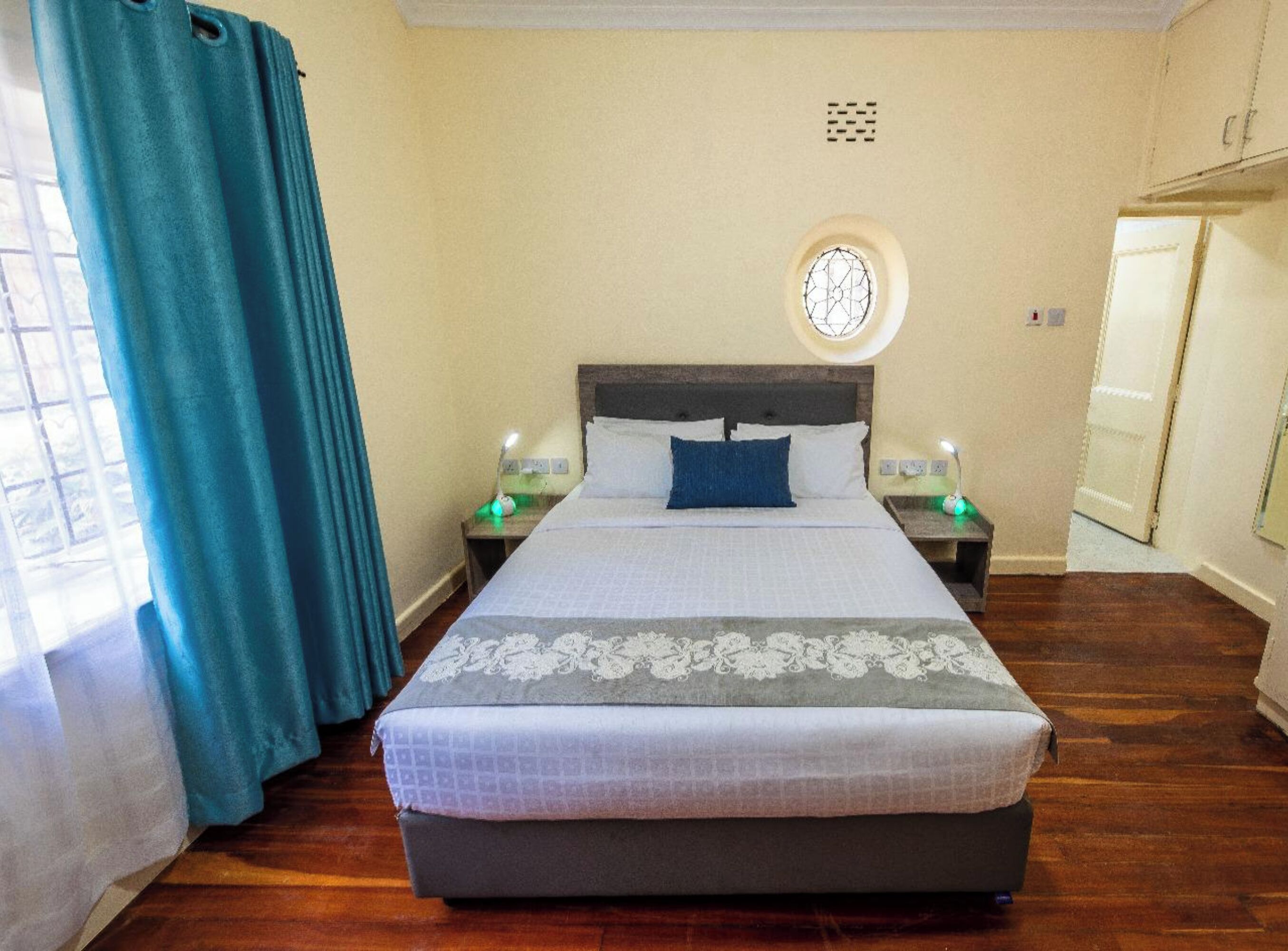 A neatly arranged hotel room with a large bed, two bedside tables, a round window, and a door.