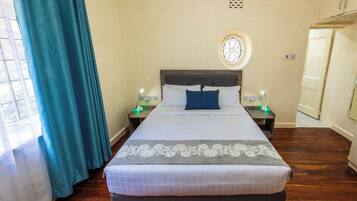 A neatly arranged hotel room with a large bed, two bedside tables, a round window, and a door.