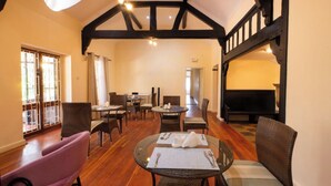 Un espace repas avec des tables rondes et des chaises en osier, un plancher en bois et un plafond haut avec des poutres apparentes.