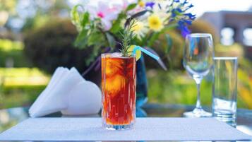 A tall glass with a red beverage, a clear glass, and a napkin on a table with a floral arrangement in the background.