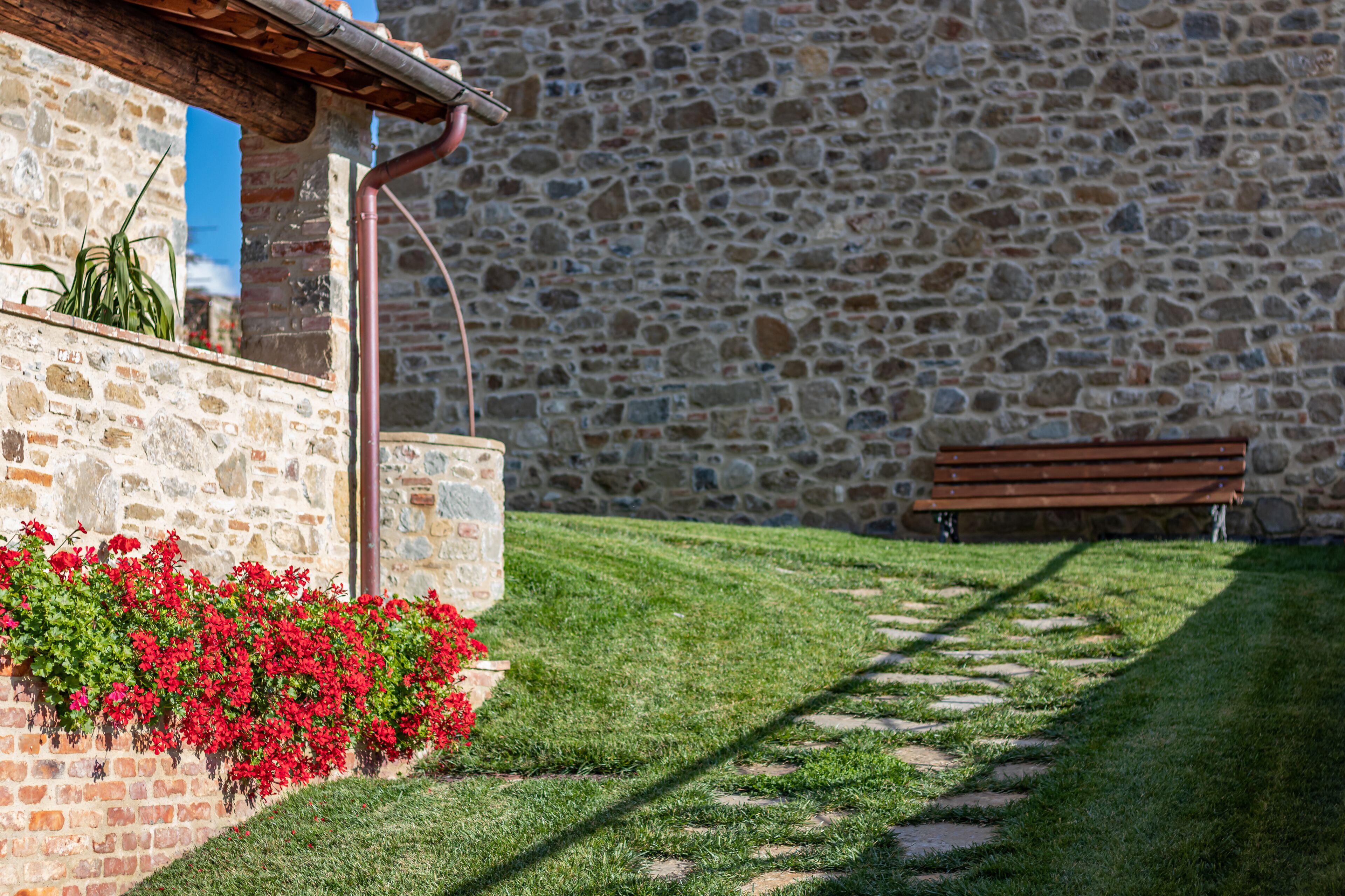 Un edificio de piedra con un muro de piedra, un banco de madera y un camino.