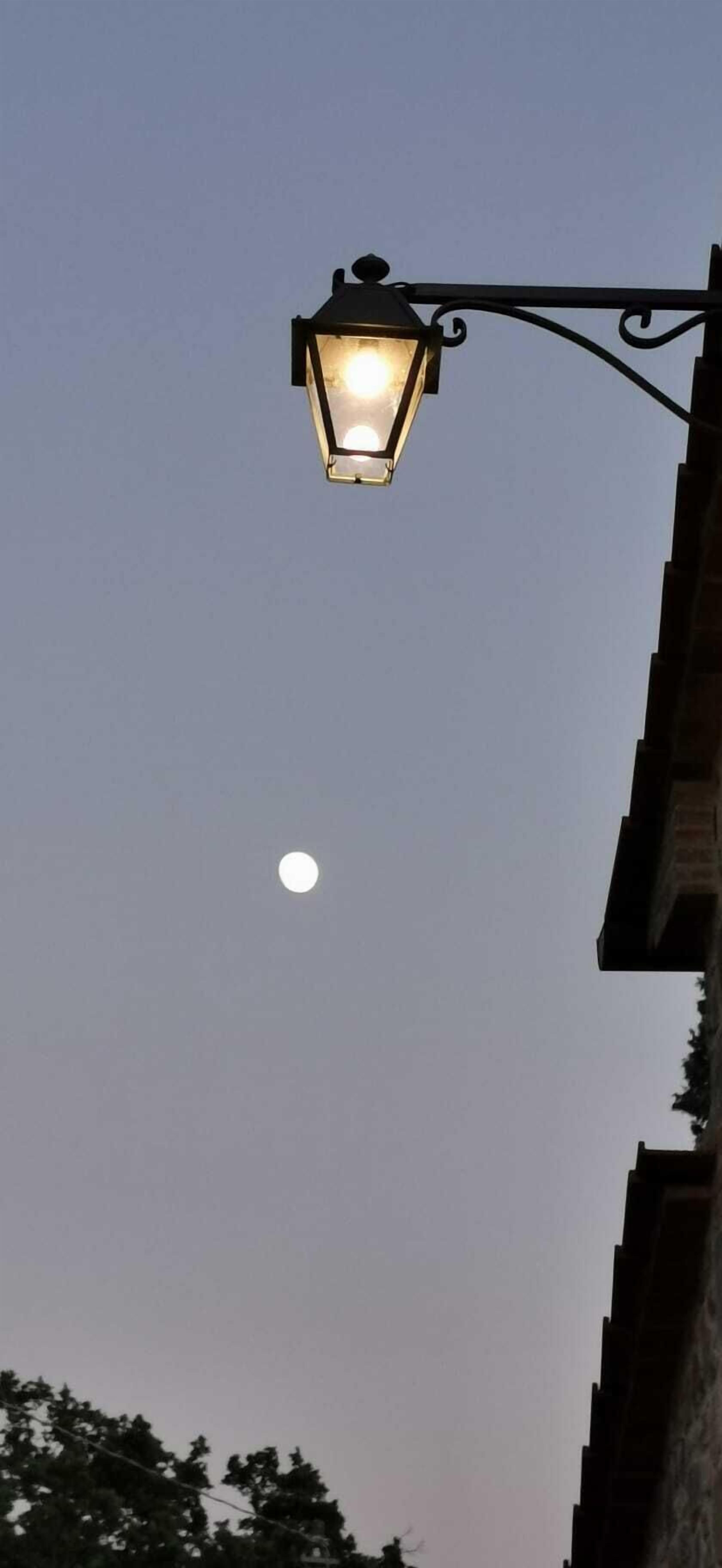 A street lamp with a clear view of the moon in the sky.
