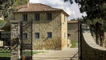 Un edificio de piedra con techo de tejas, entrada protegida por una reja y una escalera de piedra que sube.