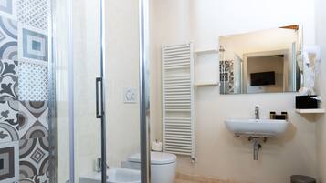 Un baño con cabina de ducha de vidrio, inodoro, lavamanos, toallero y espejo.