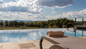 A poolside lounge with a towel, overlooking a pool with a view of trees and mountains. - Chimera Tuscany Resort (Arezzo)