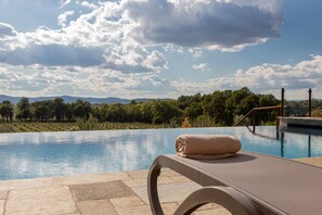 A poolside lounge with a towel, overlooking a pool with a view of trees and mountains. - Chimera Tuscany Resort (Arezzo)