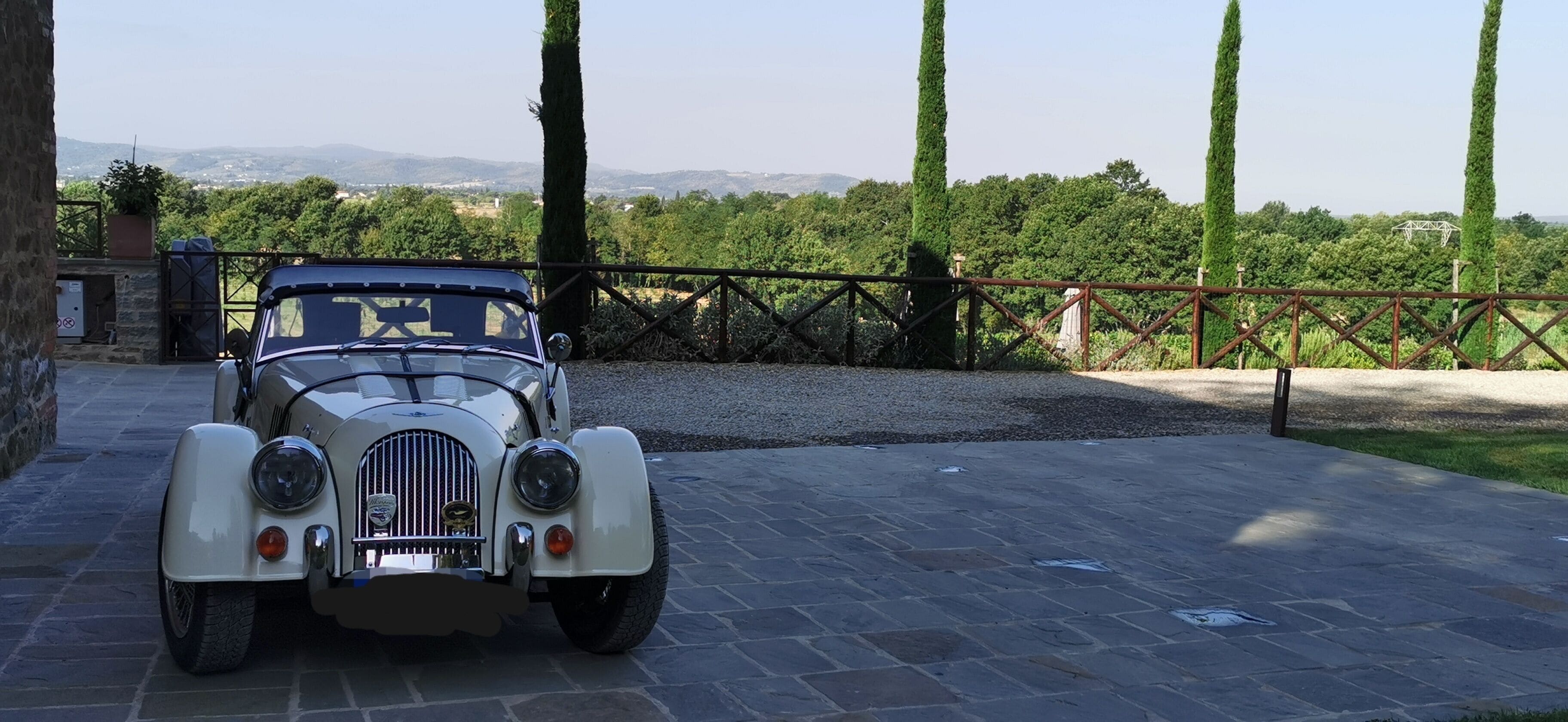 Un coche antiguo estacionado en una entrada con vistas a un viñedo y colinas al fondo.