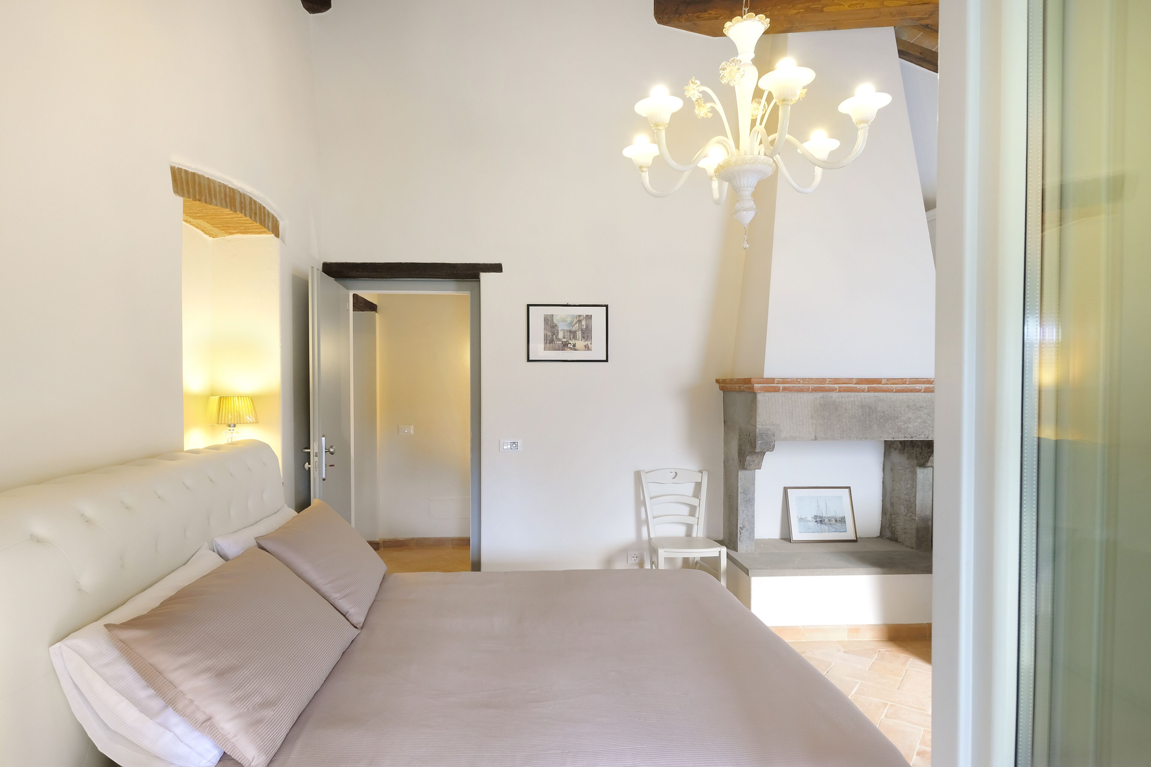 Un dormitorio con una cama grande, una silla blanca, una chimenea y un candelabro.