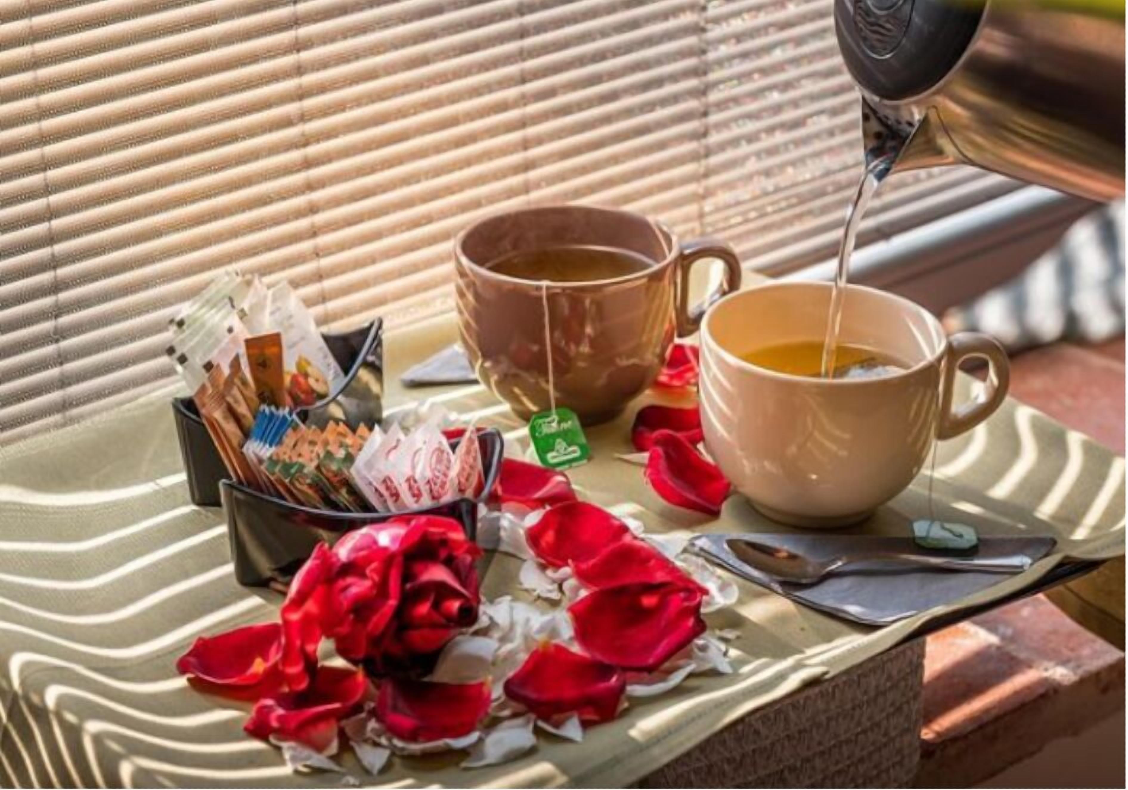 Une table avec deux tasses de thé, un sachet de thé et des pétales de rose éparpillés.