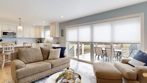 A modern kitchen with white cabinets, a dining area with a table and chairs, and a large sliding glass door leading to an outdoor patio. - On Par for the Beach (Old Orchard Beach)