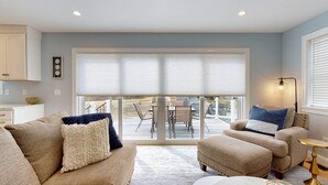 A living room with a sofa, ottoman, and a table, a balcony with a table and chairs, and a view of a garden. - On Par for the Beach (Old Orchard Beach)