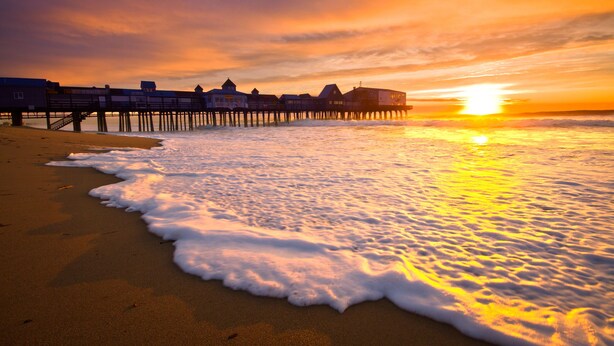 A beach with a wooden pier extending into the water, featuring several buildings with a row of windows. - On Par for the Beach (Old Orchard Beach)