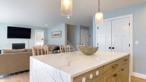 A modern kitchen with a marble island, wooden cabinets, and pendant lighting. - On Par for the Beach (Old Orchard Beach)