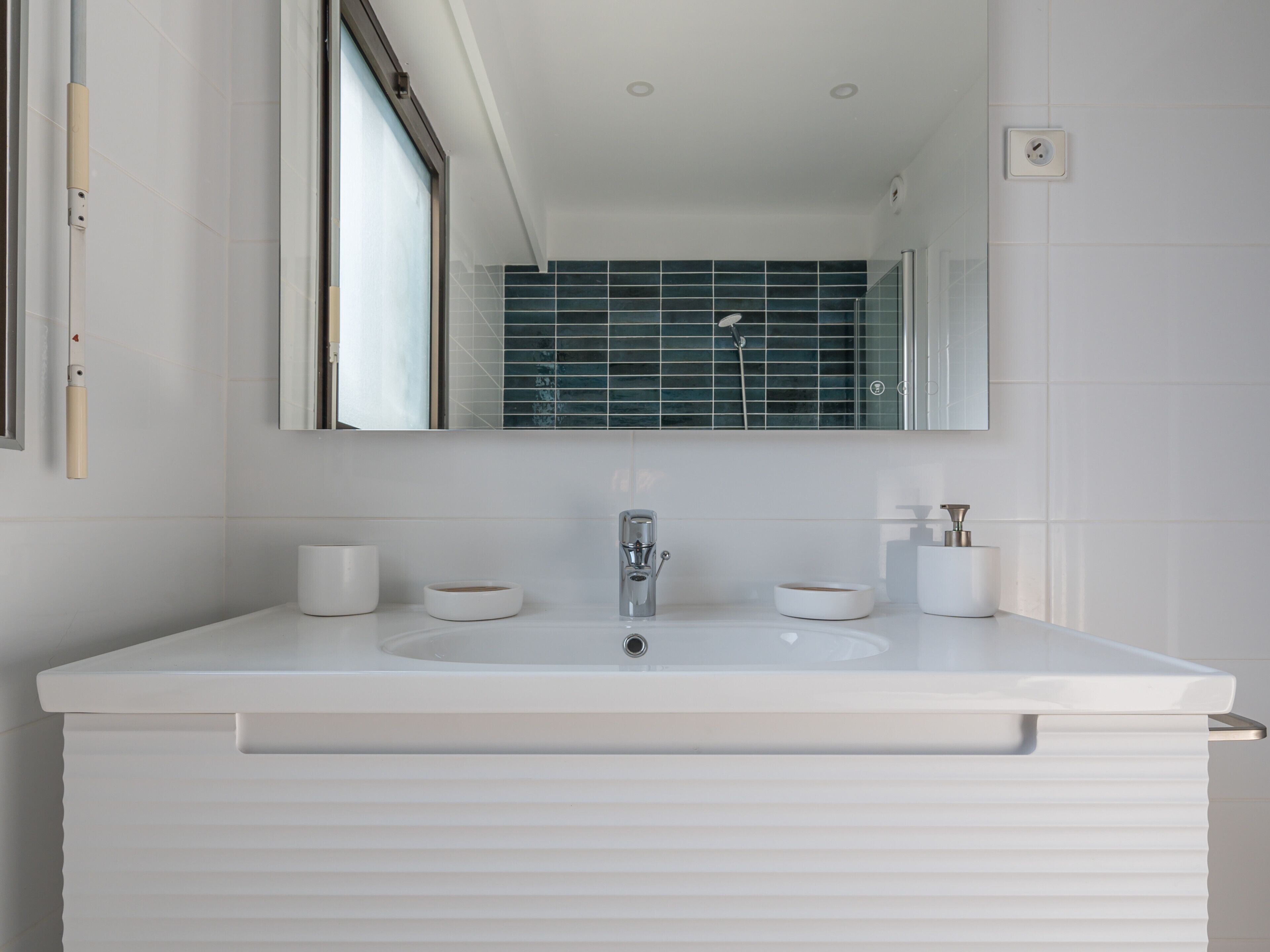A modern bathroom with a white vanity, a mirror, and a shower area.