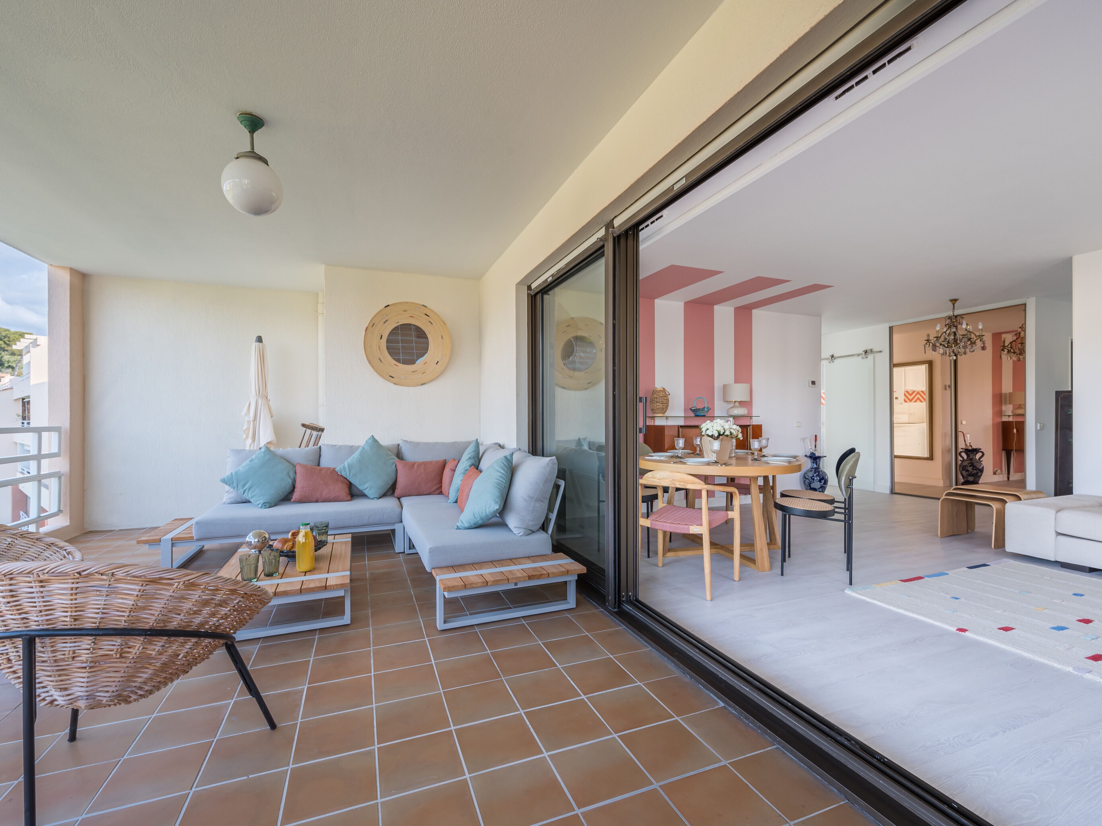 A spacious living area with a large sofa, a dining table, and a balcony with a wicker table and chairs.