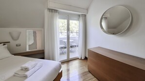 Ein Hotelzimmer mit einem Bett, einem Nachttisch, einem an der Wand befestigten Spiegel und Blick auf einen Außenbereich mit Tisch und Stühlen.