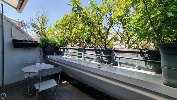 Ein Balkon mit Tisch und Stühlen, Blumentöpfen und einem Geländer.