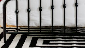 A bed with a black metal frame, white bedding, and a red blanket. There are two pillows with a zigzag pattern. A lamp and a small plant are on a bedside table. - Come back to peace after busy days at Maxwell or downtown. (Montgomery)