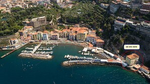 Vista aérea de un pueblo costero con un puerto deportivo, edificios y un acantilado.