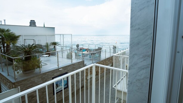 Un balcón con vista al mar, plantas en macetas y mobiliario de exterior.