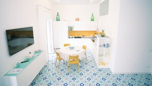 Una cocina compacta con comedor, que presenta piso de baldosas, muebles blancos y una pequeña isla con pileta.