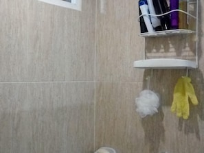A bathroom with a tiled wall, a white shelf with toiletries, and a yellow glove hanging on the wall.