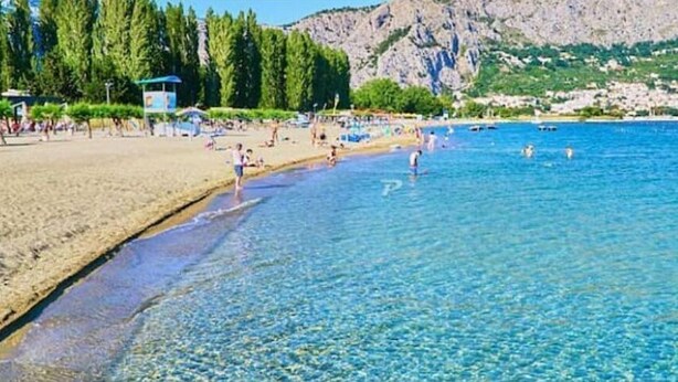 Ein Strand mit klarem Wasser, badenden Personen und einem Rettungsturm.