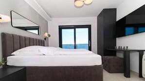 Ein modernes Schlafzimmer mit einem großen Bett, einem kleinen Tisch, einer Bank und Meerblick durch eine Schiebetür.