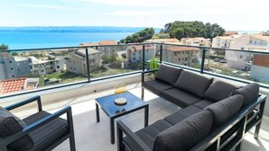 Ein Balkon mit einer Couch, einem kleinen Tisch und Blick auf das Meer und Gebäude.