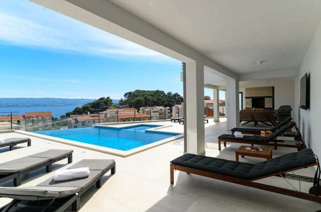A modern outdoor pool area with lounge chairs and a view of the sea.