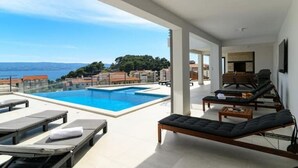 Ein moderner Poolbereich im Freien mit Liegestühlen und Blick auf das Meer.