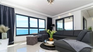 Ein modernes Wohnzimmer mit einem großen Fenster, einem grauen Sofa, einem Couchtisch und einer Topfpflanze.