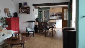 A living room with a wooden floor, a red cabinet, a dining table with chairs, and a kitchen area in the background. - A 1h de Paris, et 1h des Châteaux de la Loire, (CHALETTE SUR LOING)
