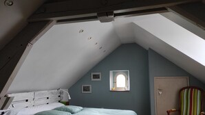 A bedroom with a sloped ceiling, a bed with green bedding, a small window, a door, and a striped chair. - A 1h de Paris, et 1h des Châteaux de la Loire, (CHALETTE SUR LOING)