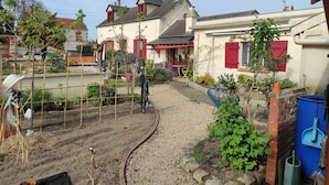 A residential garden with a gravel path, a small brick wall, and a variety of plants. - A 1h de Paris, et 1h des Châteaux de la Loire, (CHALETTE SUR LOING)