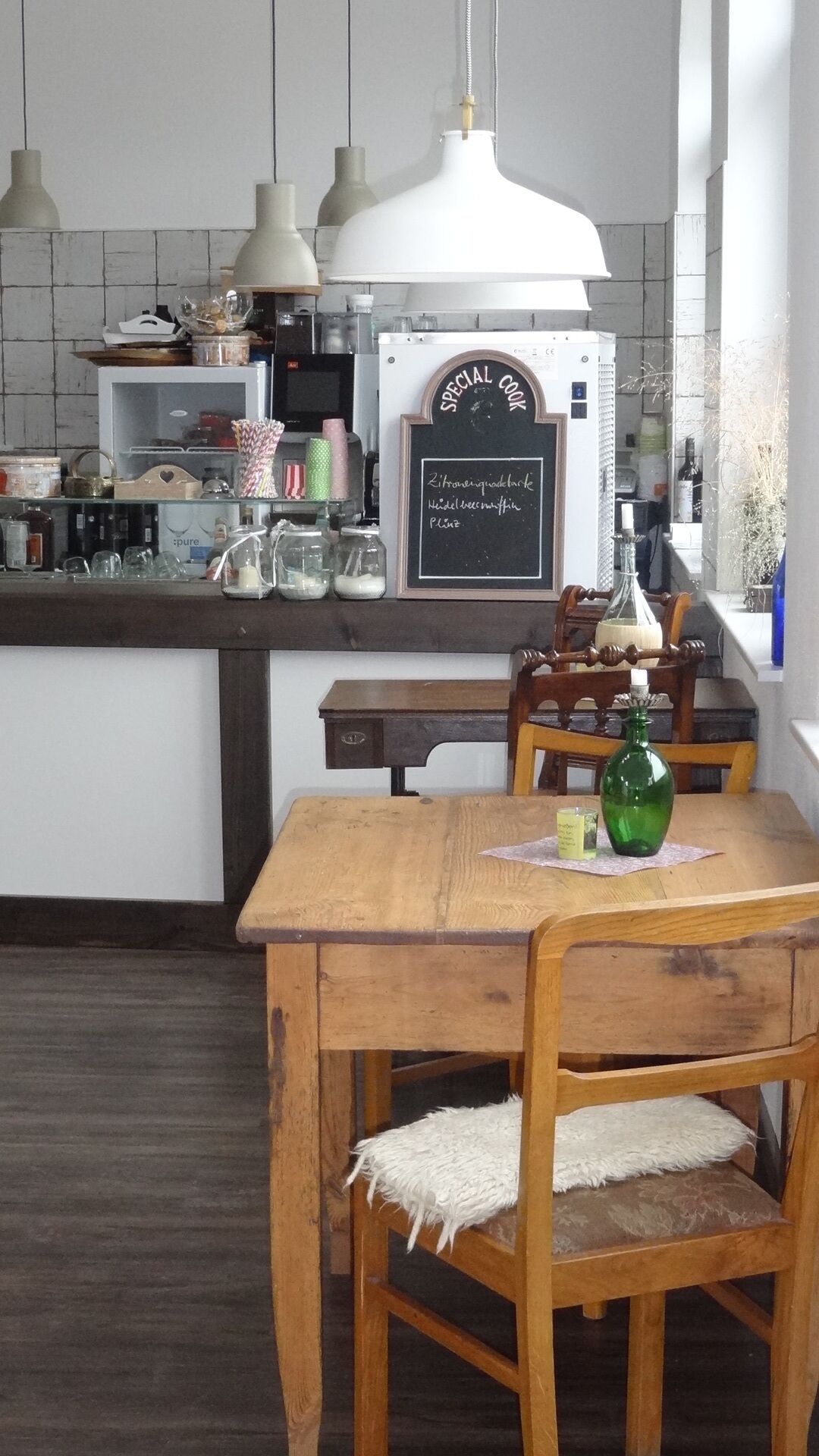 A kitchen with a wooden table and chairs, a chalkboard sign, and various kitchen items.
