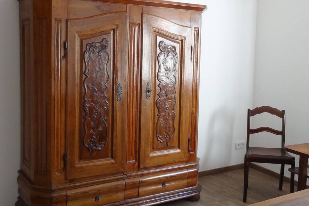 Un dormitorio con un armario de madera, una cama de madera y una silla de madera.