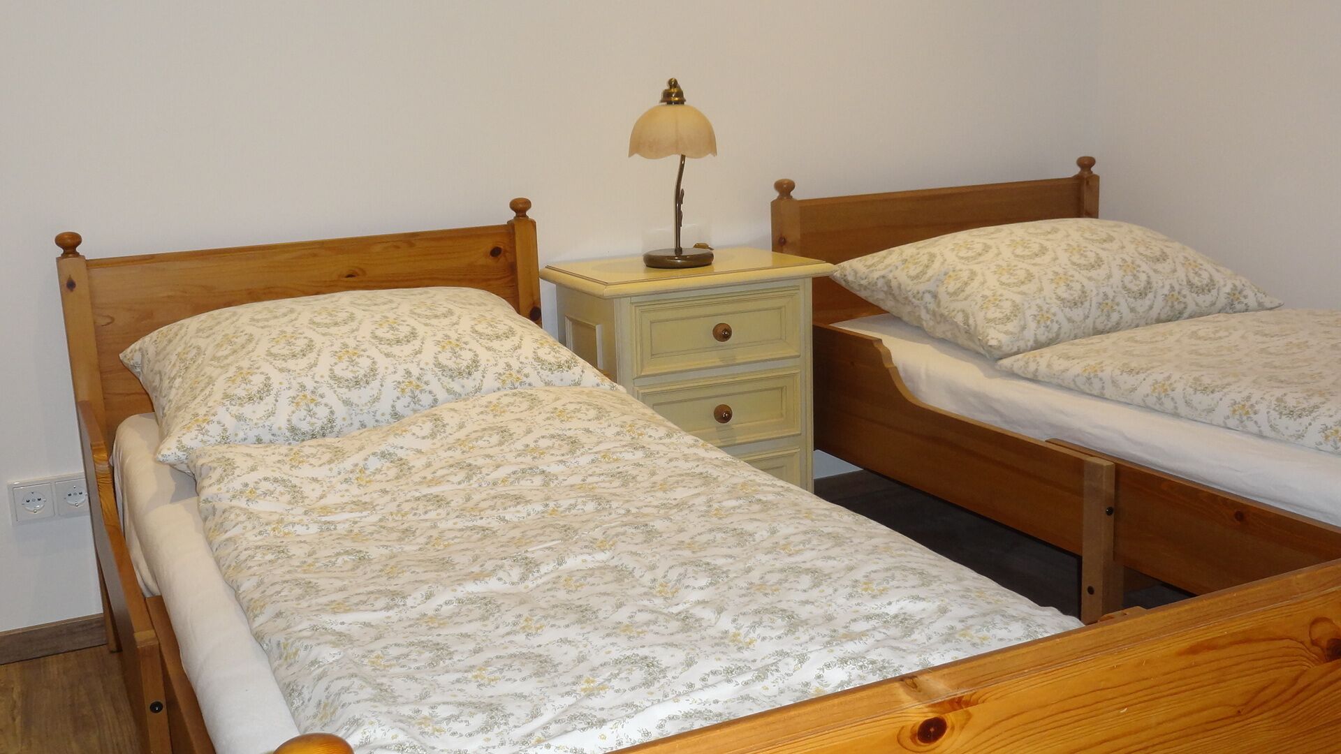 Una habitación con dos camas de madera, cada una con cabecera y piecera a juego, y una mesita de noche con una lámpara.