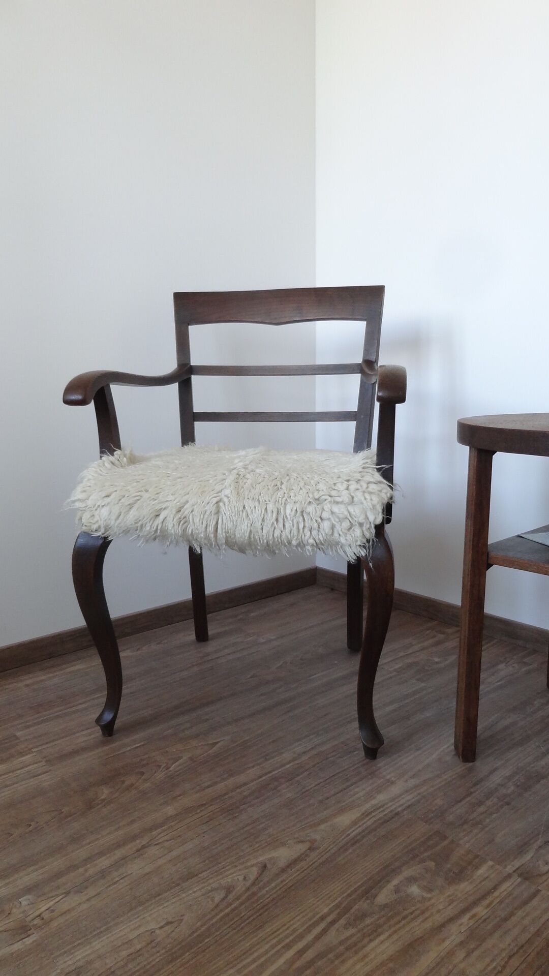 Ein Holzhocker mit einem flauschigen Kissen in einem Raum mit Holzboden und einer schlichten Wand.